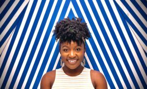 Woman smiling in front of a blue stripped wall.